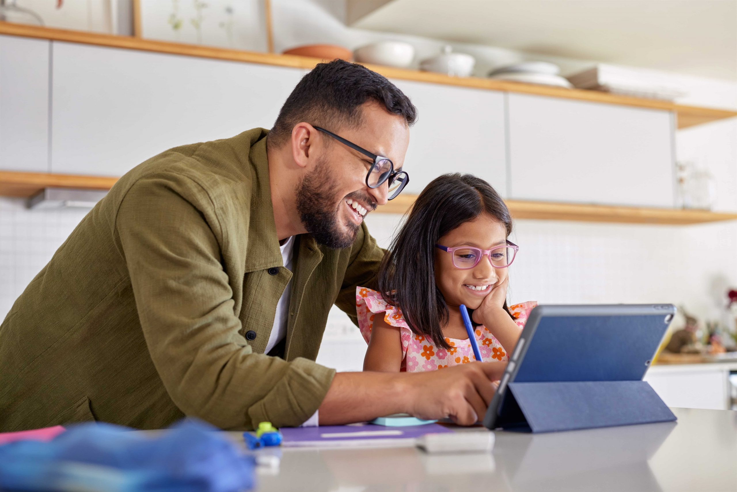 Father and daughter sitting at a tablet in a kitchen.